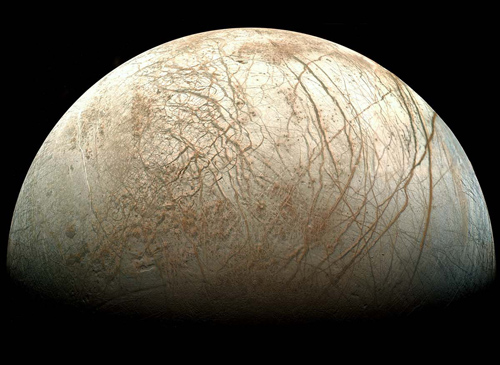 Europa, as viewed from NASA’s Galileo spacecraft. Visible are plains of bright ice, cracks that run to the horizon, and dark patches that likely contain both ice and dirt. Image reprocessed by Ted Stryk.