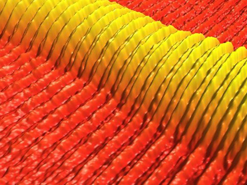 This atomic force microscope image shows directed self-assembly of a printed line of block copolymer on a template prepared by photolithography. The microscope’s software colored and scaled the image. The density of patterns in the template (bounded by the thin lines) is two times that of the self-assembled structures (the ribbons). Image courtesy of Serdar Onses/University of Illinois-Urbana