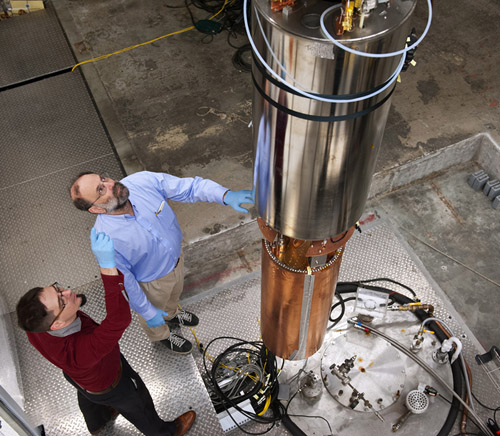 University of Washington physicists Leslie Rosenberg (right) and Gray Rybka examine the experiment package as it is positioned above the bore of a large superconducting magnet, two primary components of the detector being used in the Axion Dark Matter Experiment. The components were assembled in mid-October and lowered into the magnet bore (lower right) to begin the detector’s commissioning phase. Image credit: Mary Levin / University of Washington
