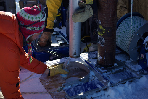 Water from the Greenland perennial firn aquifer draining from a core extracted 12 m below the surface of the ice sheet. The core was drilled in April, months prior to seasonal melt, with air temperatures -15 C confirming the water was retained at depth throughout the winter. Clément Miège is pictured collecting a sample of the water. Photo Credit: Ludovic Brucker