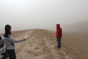 During a windstorm on China’s Loess Plateau, geoscientist Fulong Cai uses a plastic bag as a wind sock to show that the wind blows parallel to the linear ridge he and Wang Zhao are standing on. Roads in this area run along the ridges. (Photo Credit: Paul Kapp/ UA Department of Geosciences)